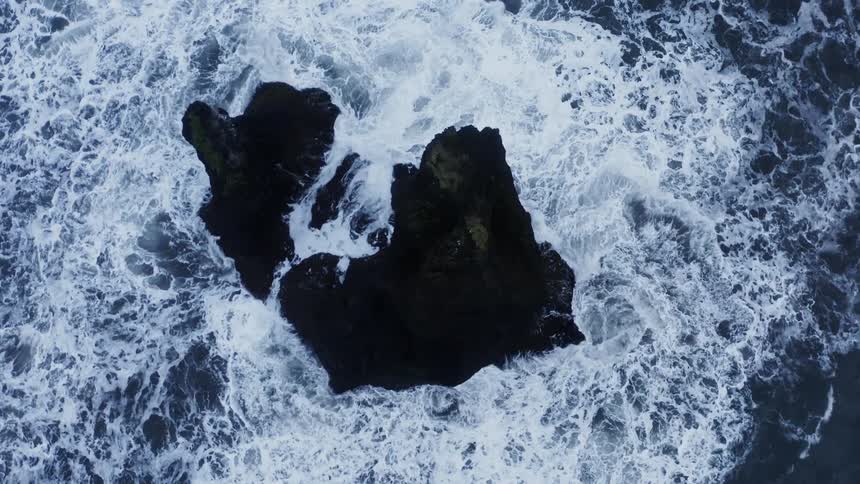 Ocean waves crash and churn against tall rocky island