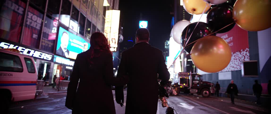 A man holding balloons walks with a woman