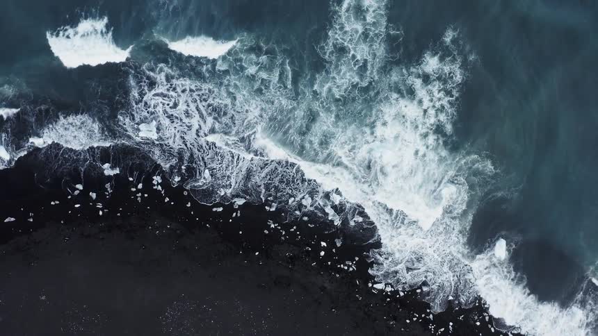 Aerial view of ocean waves crashing on the black sand of a beach
