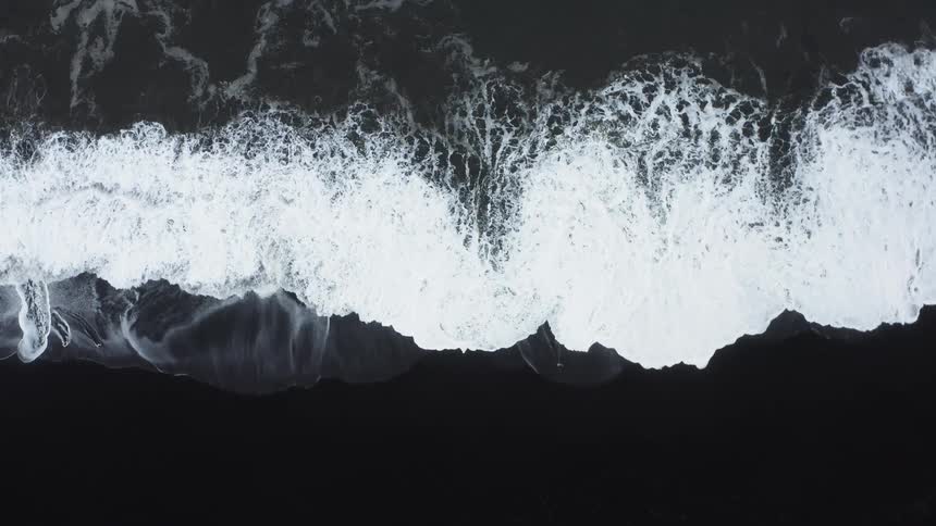 A beach with water waves and sand with birds flying in the air