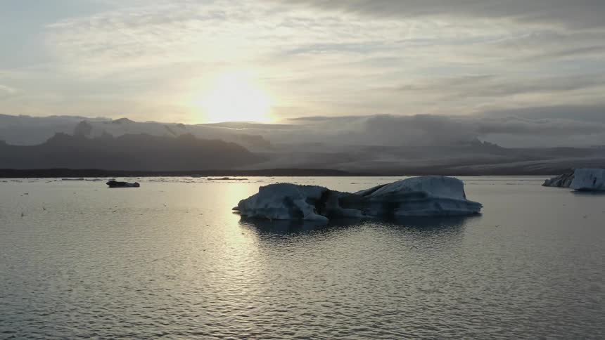Icebergs floating in the ocean near the mountains at sunset