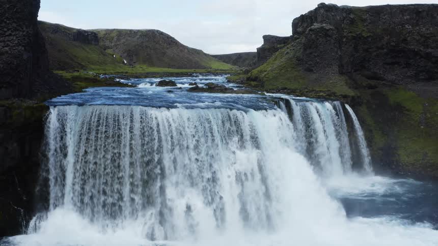 A short waterfall empties into a river in a canyon