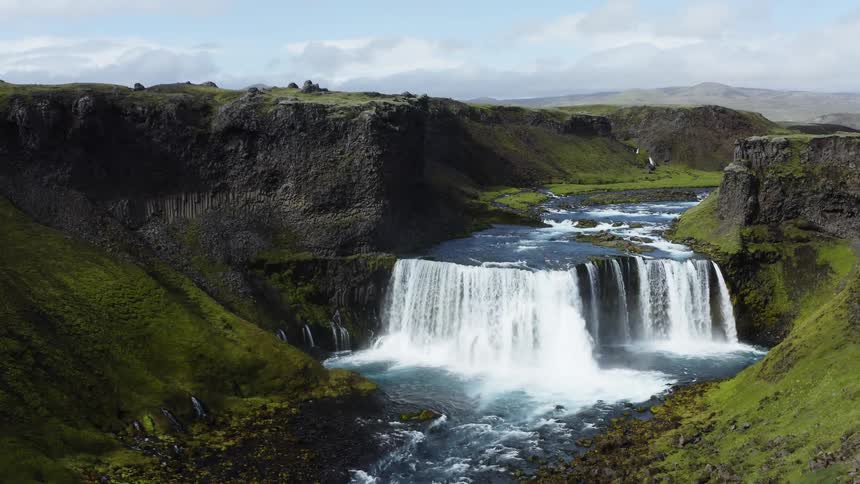 Whitewater flows down a river and over a waterfall surrounded by green rocky cliffs
