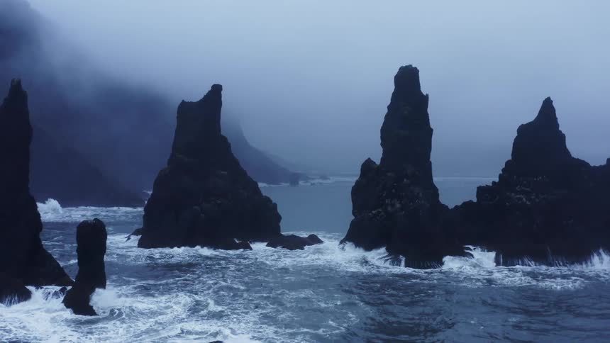 A rocky coast with water and waves with fog with the sky and clouds in the background