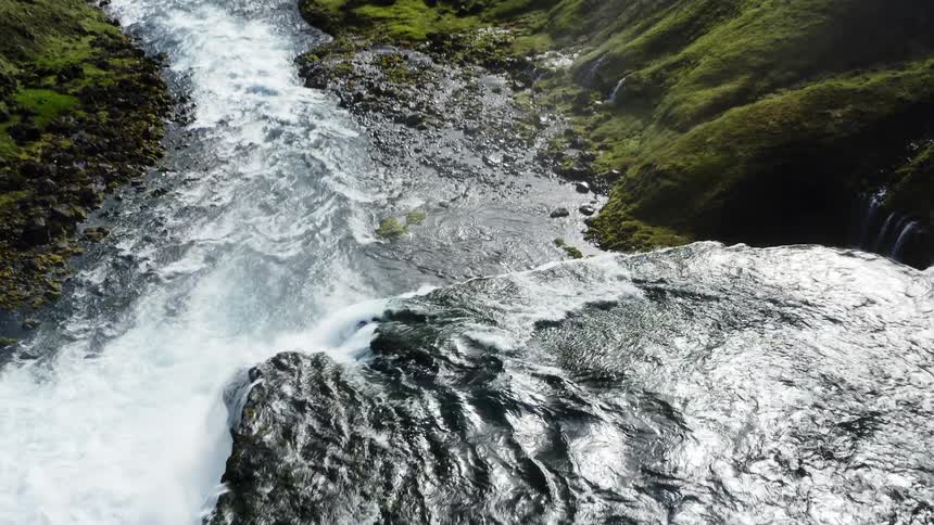 Aerial view of a river turning into a waterfall on the green hills near the mountains