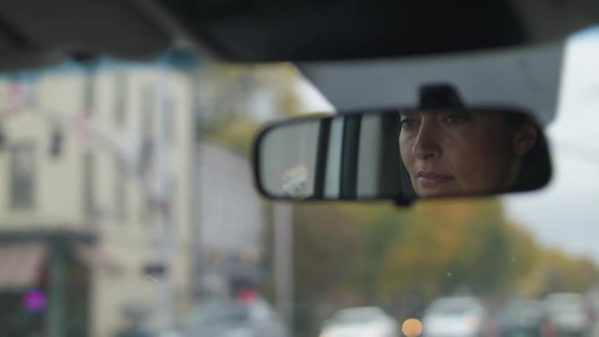 Reflection of a woman face on the rearview mirror of a car driving through town