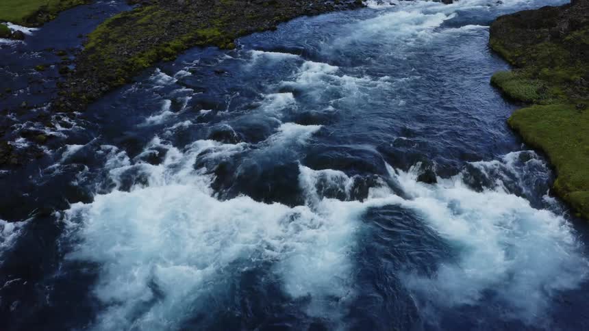 Aerial view of a river flowing over the rocks on the green landscape