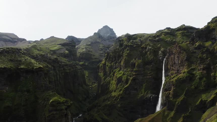 A bird flies out of a mountain range as waterfalls flow down the side of a mountain