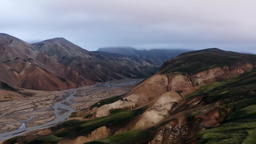 An aerial view of a mountain range with a winding river in a wide valley and grassy plateaus