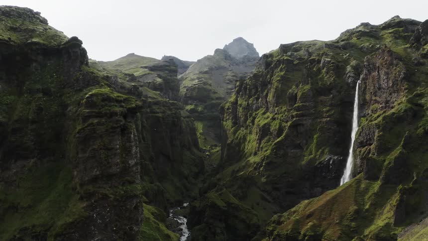 A canyon with a river and a waterfall with the sky and clouds in the background