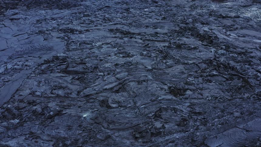Gray dried volcano ash and cooled magma with flow lines cover ground