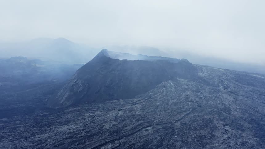 A volcano with smoke with a mountain range the sky and clouds in the background