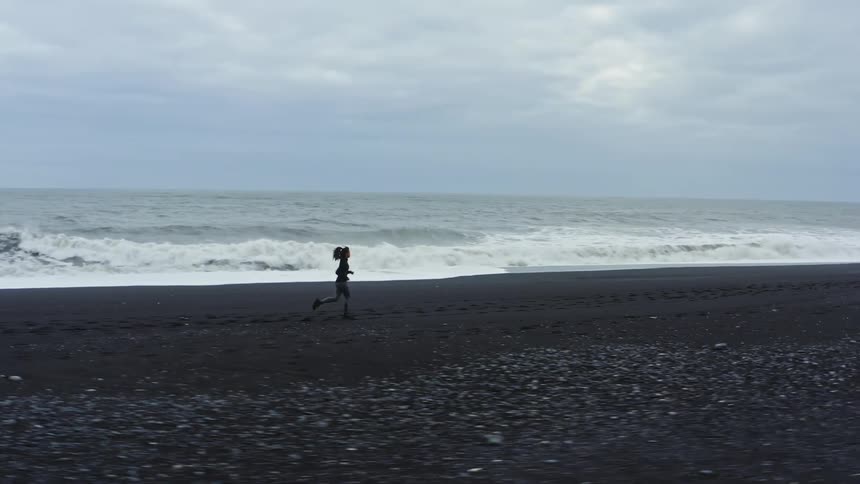 A woman is jogging across a beach as waves roll over the sand