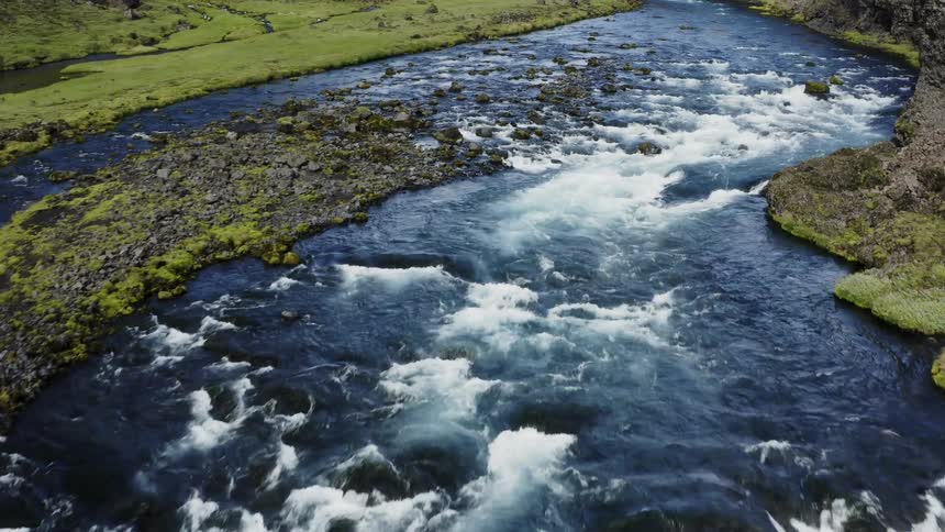 River water flows between slopes and steep cliff around island and down rapids