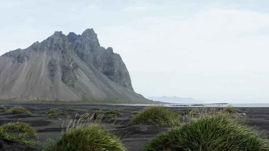 A person running on a landscape near a coast with a mountain range the sky and clouds in the background