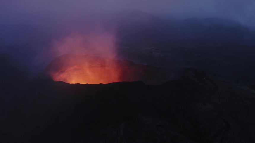 Aerial view of active volcano with a large opening at the top through which gases and lava are forced out