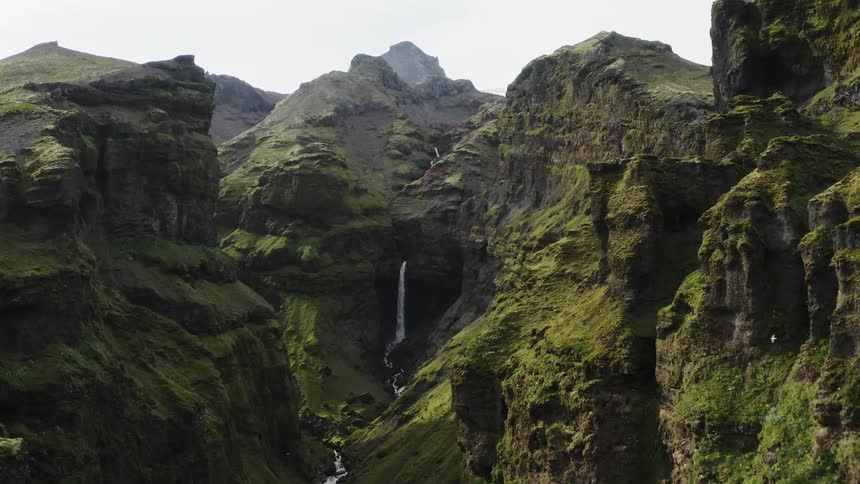 Aerial view of a waterfall flowing inside the green gliff walls of a gorge