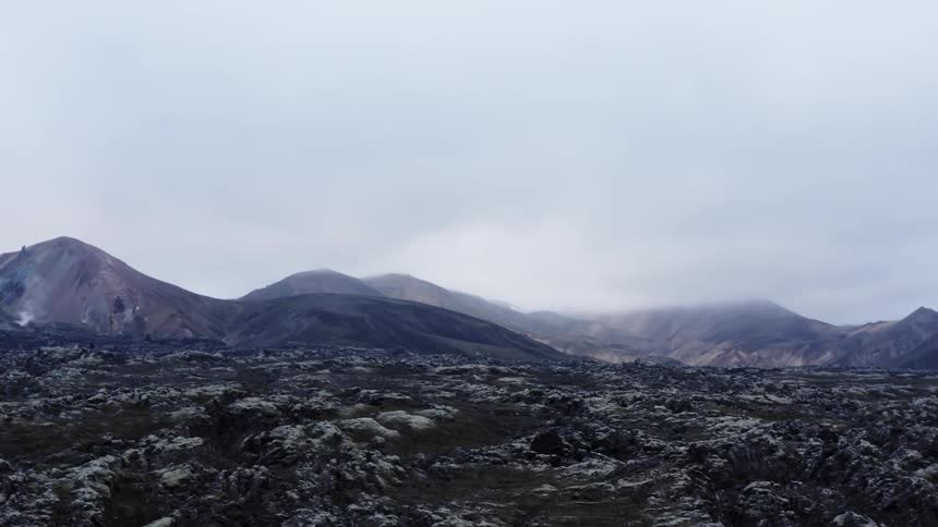 View of volcanic field and distant mountains under cloudy sky