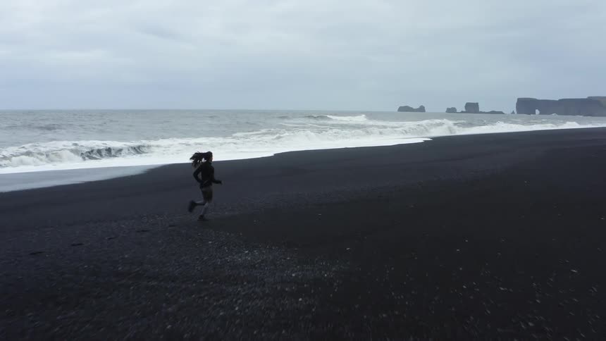 A woman runs along the beach as the waves from the ocean crash towards the shore