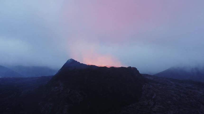 A volcano crater glows in the fog