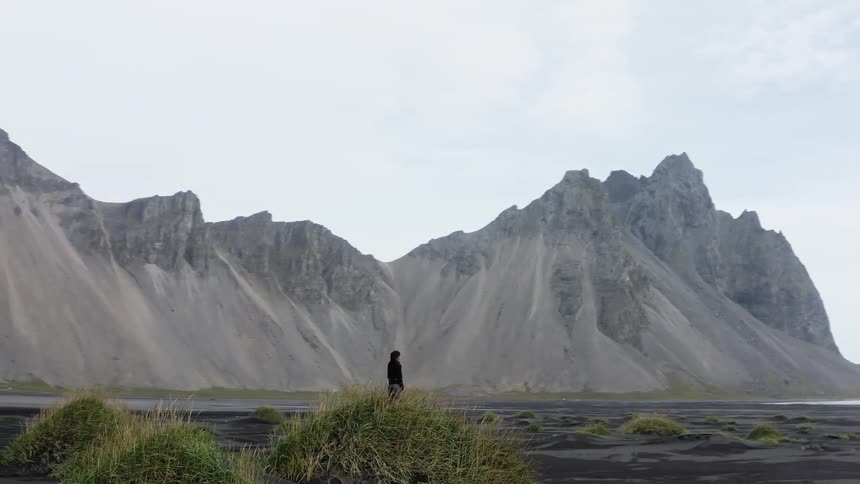 Man standing on a grassy mound on a volcanic field near the mountains