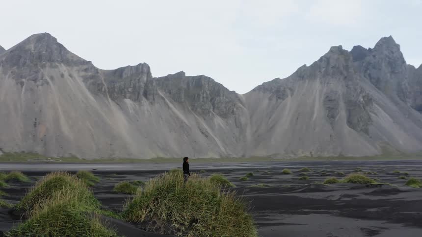 A person stands on the shore in front of a mountain and looks in to the distance