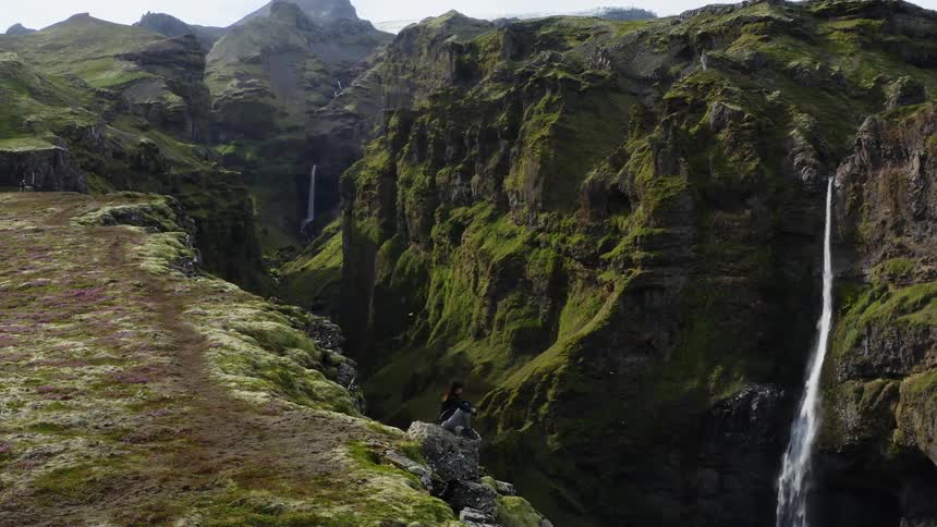 A person sitting on a boulder near a gorge in front of a waterfall