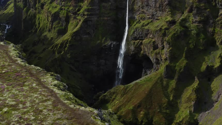 Aerial view looking down a ravine in the mountains as birds fly near a waterfall
