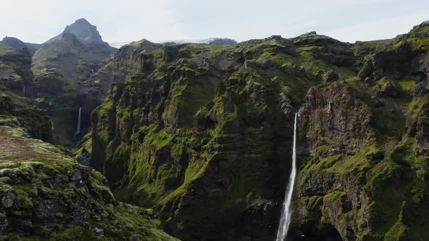 Aerial view of man sitting on rock looking at high mountains with waterfall cascading down the mountainside
