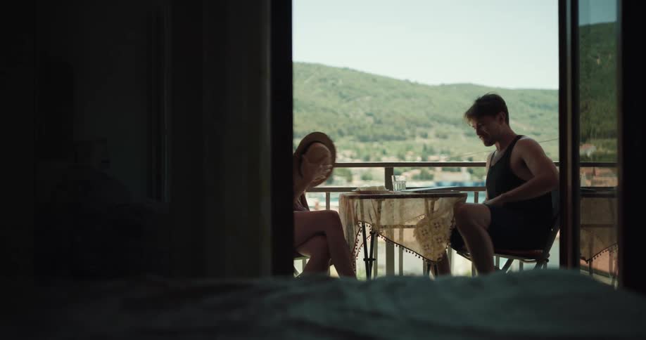 Young couple sitting on a table on the apartment balcony stand up and run inside
