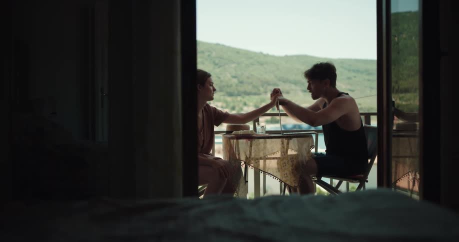A man and a woman on a balcony arguing with the man talking on a smartphone with the sky and clouds in the background