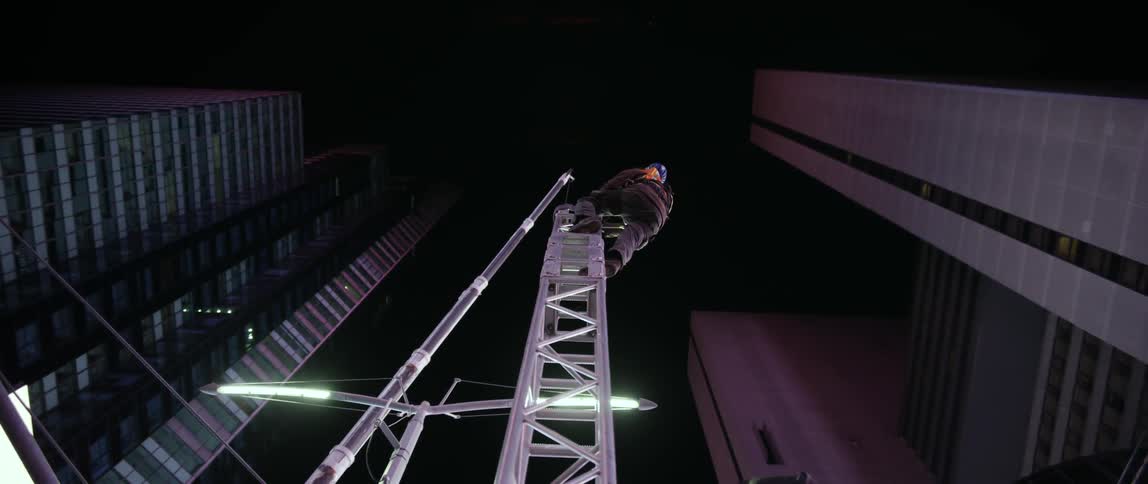 A man climbs a tall metal tower in a city sky