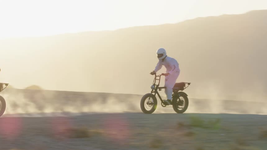 Two teenagers kick up dirt as they ride bicycles through the desert
