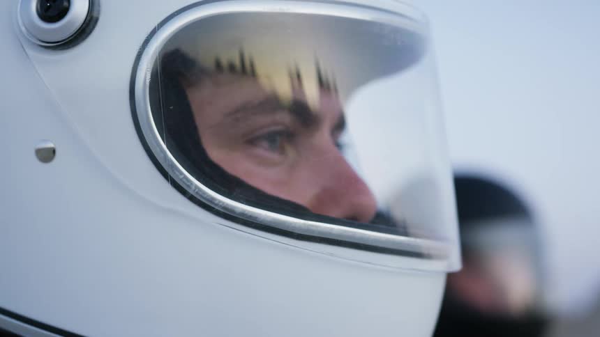 The sun sky and rock formations are reflected on the face visor of a man wearing a white helmet