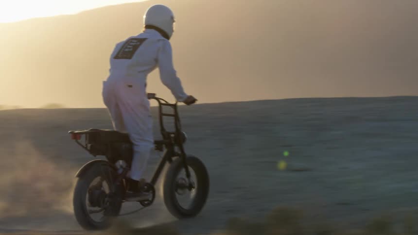A motorcyclist rides a dirt bike through arid terrain in the desert during the day
