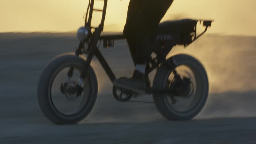 A person is riding a small motorcycle in a dirt lot at sunset