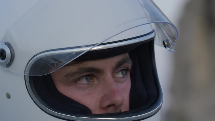 A man with a helmet lifting up his visor with the sky and clouds in the background