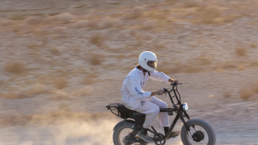 A motorcyclist rides a dirt bike through arid terrain in the desert during the day