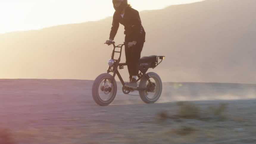 A man stands as he rides a bicycle through the desert