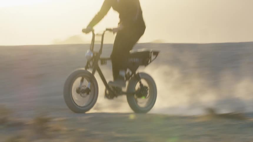 A person with a helmet riding a motorcycle in a desert with the sky and clouds in the background
