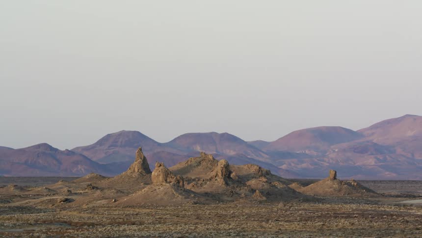 A desert landscape with hills with a mountain range the sky and clouds in the background