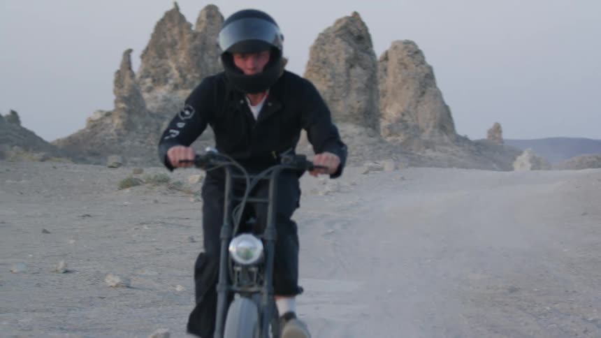 A man leaves a dust trail riding a motorbike in a desert