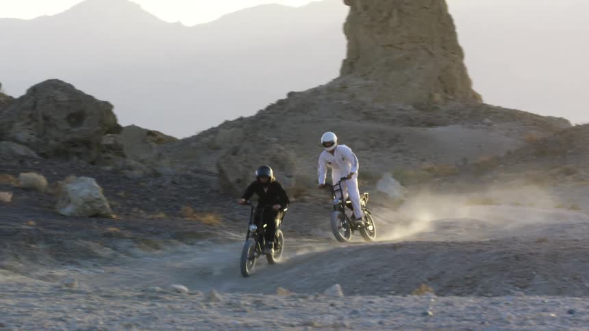 People wearing black and white overalls and crash helmets driving motorcycles on the desert