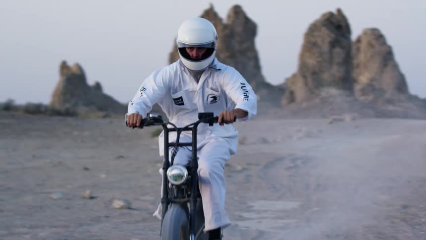A man in a white jumpsuit and helmet rides a dirt bike through the desert