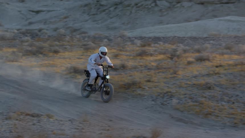 Man wearing a white suit and crash helmet drives a motorcycle on a road desert