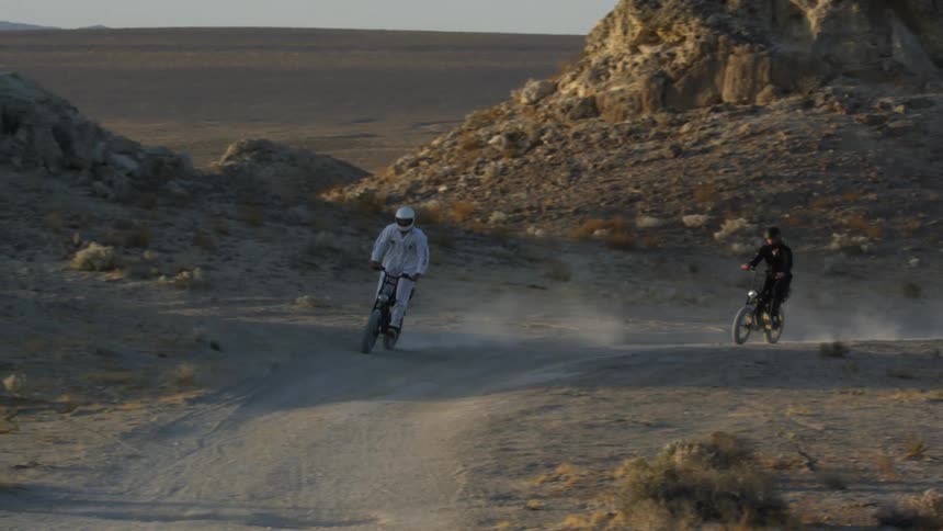Two cyclists stand on their bikes as they ride through the desert