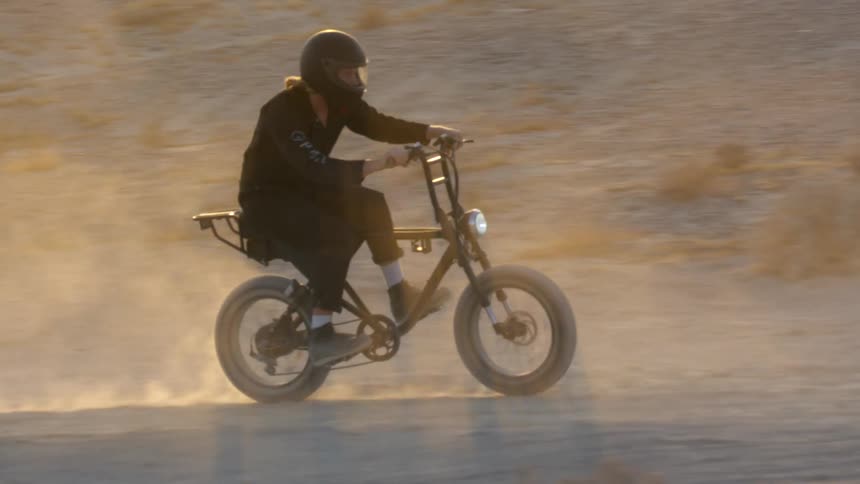 A motorcyclist rides a dirt bike offroad through the desert during the day