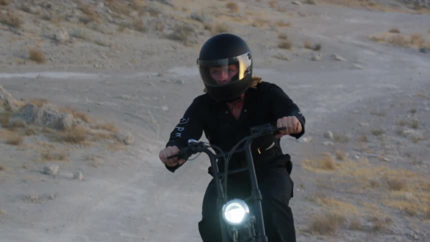 A person with a helmet riding a motorcycle on a dirt road with the sky and clouds in the background
