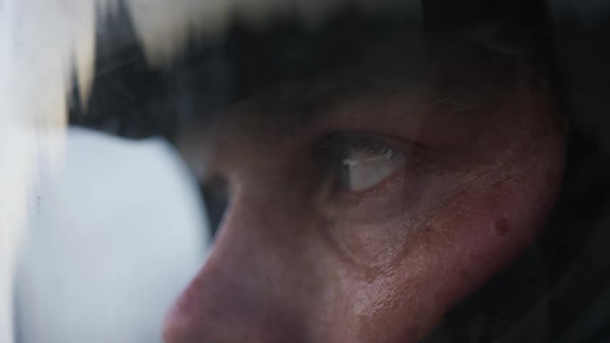 The surrounding landscape is reflected on the visor of a helmet worn by a man