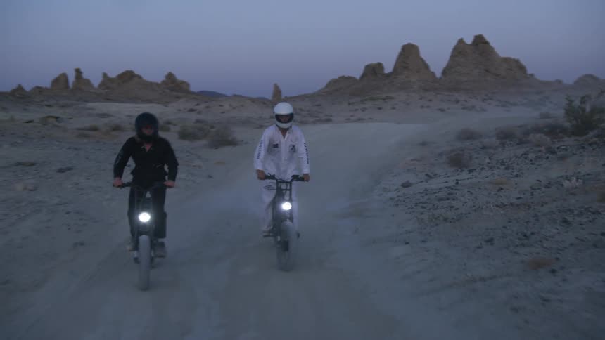 Two people riding dirt bikes on a trail in a desert